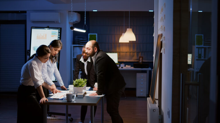 Multi ethnic businesspeople lean on conference table analyzing company strategy ideas overworking at management presentation. Diverse teamwork brainstorming financial solution in meeting room